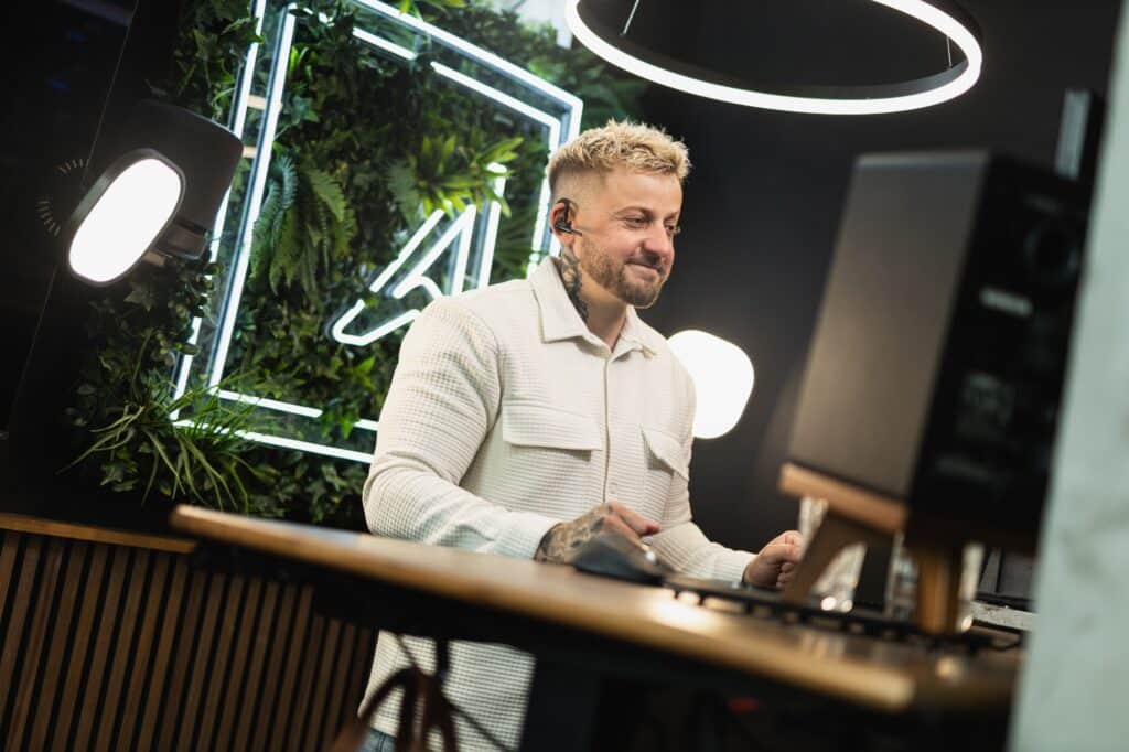 Sascha Hahne am Schreibtisch vor der leuchtenden Logo-Wand der Agentur Ausdruckslos
