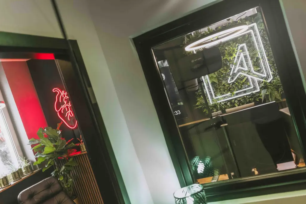 Blick durch die Glastür auf die Pflanzenwand mit Logo und das Neon-Herz im Büro der Agentur Ausdruckslos